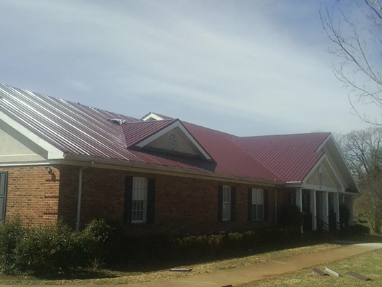 Red metal roof with gabled entries on a long brick building, from a Hail Damage Roof Repair job in Marion